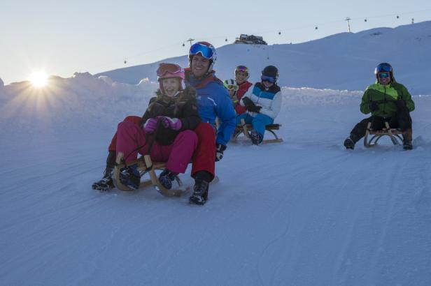 Eine Gruppe von Menschen rodeln auf einer schneebedeckten Piste.