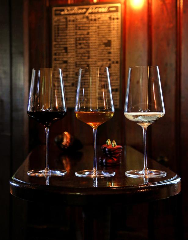 Drei Weingläser gefüllt mit Rotwein, Weißwein und Roséwein stehen auf einem Tisch.