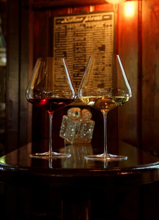 Zwei Weingläser, eines mit Rotwein und eines mit Weißwein, stehen auf einem Tisch.