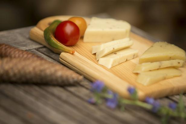Käse, Tomaten und eine grüne Chili liegen auf einem Holzbrett.