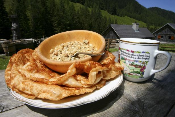 Eine Mahlzeit mit Krapfen, einer Schüssel mit Graupen und einer Tasse vor einer Bergkulisse.