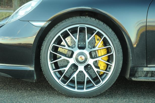 Detailansicht des Rads eines schwarzen Porsche mit gelben Bremssätteln.
