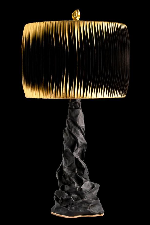 Eine dekorative Lampe mit einem schwarzen Lampenschirm und einem ungewöhnlichen, skulpturalen Fuß.