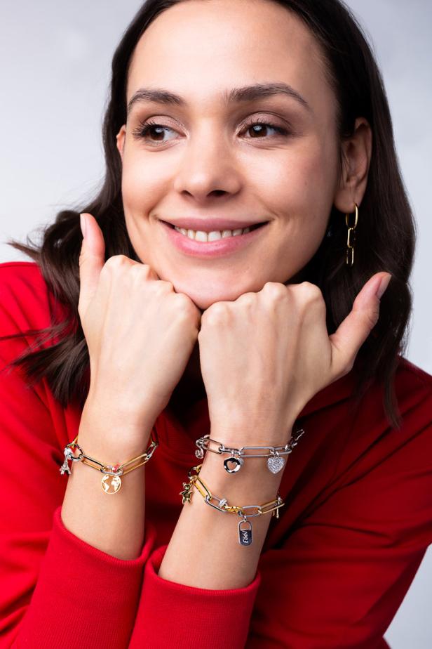 Eine lächelnde Frau präsentiert Armbänder mit Anhängern.