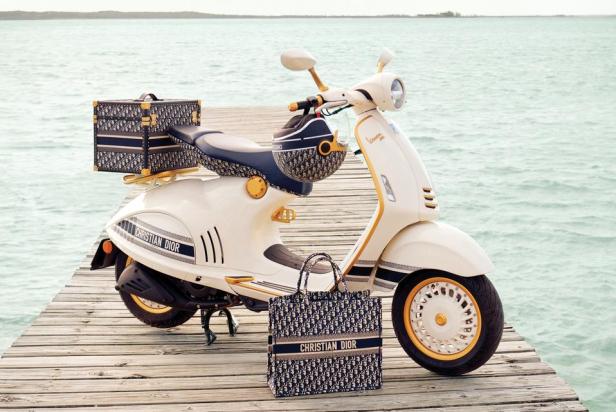 Eine weiße Vespa, geschmückt mit „Christian Dior“-Accessoires, steht auf einem Holzsteg am Meer.