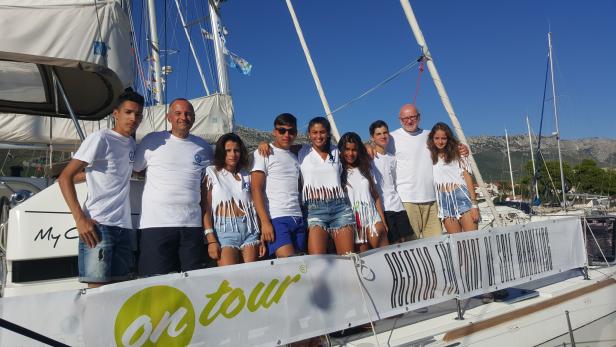 Eine Gruppe junger Leute posiert auf einem Segelboot für ein Foto.