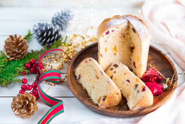 Ein angeschnittener Panettone auf einem Holzteller mit weihnachtlicher Dekoration.
