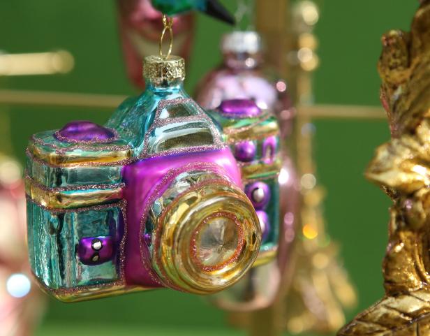 Ein bunter Christbaumschmuck in Form einer Kamera hängt an einem Weihnachtsbaum.