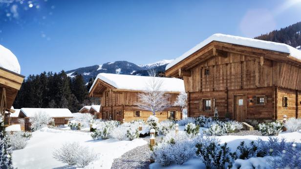 Verschneite Holzhäuser in einer Winterlandschaft unter blauem Himmel.