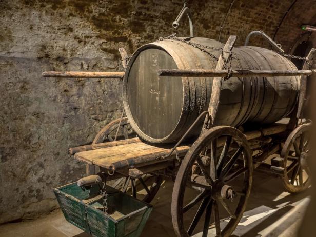 Ein alter Holzwagen mit zwei großen Weinfässern in einem Keller.