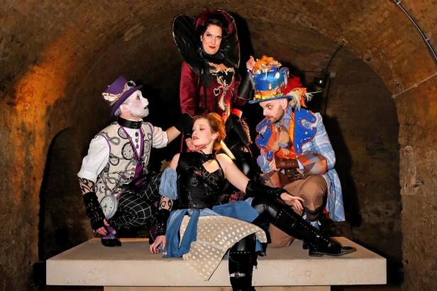 Eine Gruppe von Personen in Kostümen, die an „Alice im Wunderland“ erinnern, posiert in einem Keller.