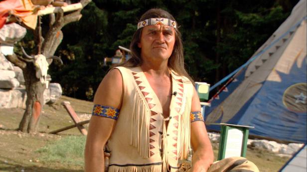 Ein Mann in traditioneller indianischer Kleidung steht vor einem Tipi.