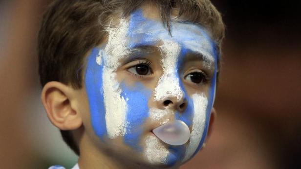 Ein Junge mit blau-weiß bemalten Gesicht bläst eine Kaugummiblase.
