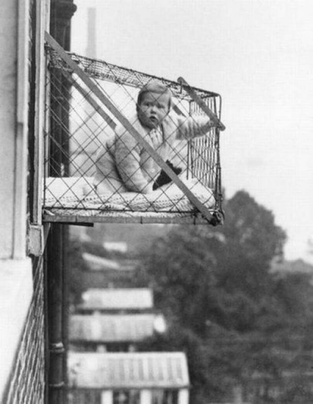 Ein Baby sitzt in einem Käfig, der an einem Fenster befestigt ist.