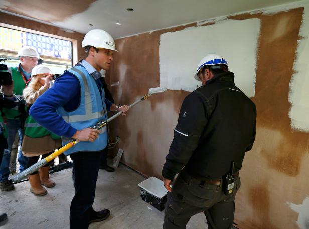 Prinz William streicht mit einer Farbrolle eine Wand in einem Raum.
