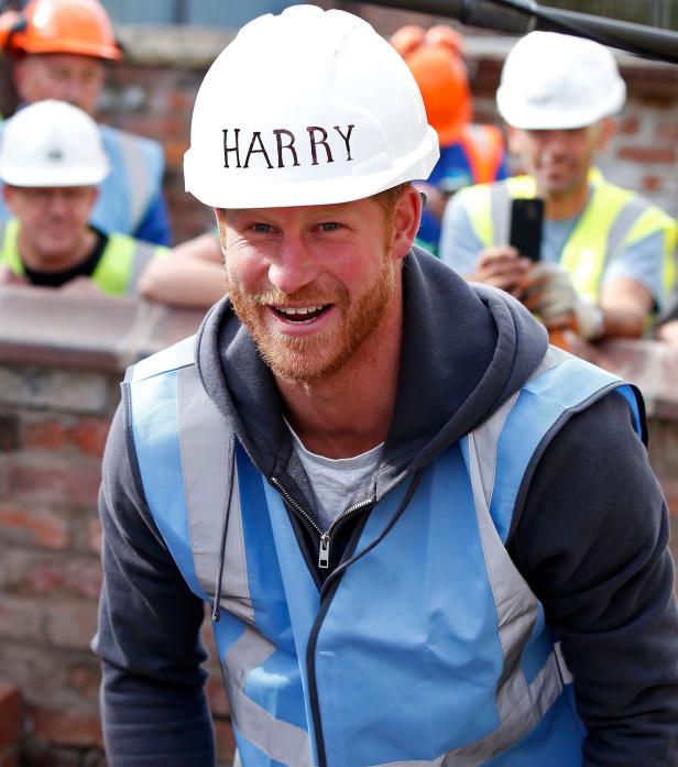 Prinz Harry trägt einen Bauhelm mit seinem Namen und lächelt.