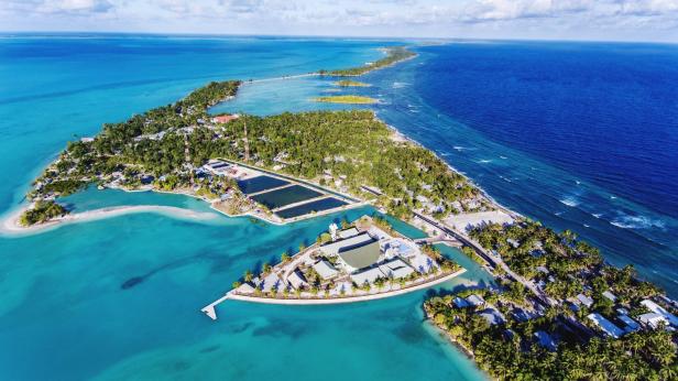 Luftaufnahme eines tropischen Atolls mit türkisfarbenem Wasser und üppiger Vegetation.
