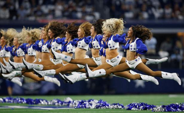Eine Reihe Cheerleader der Dallas Cowboys springen synchron in die Luft.