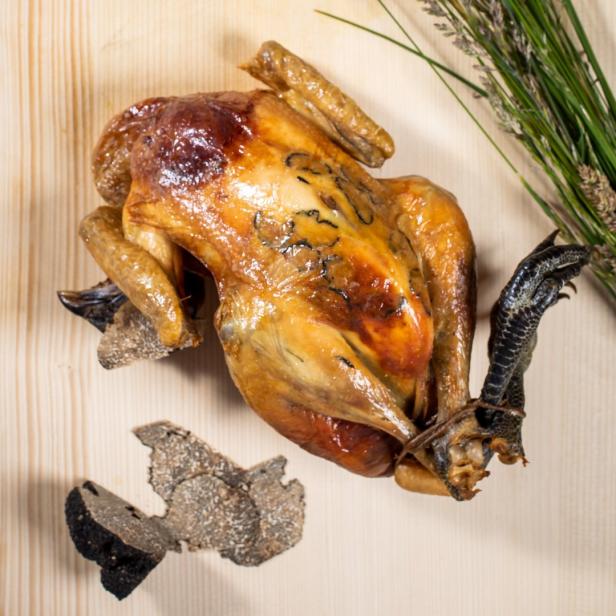 Ein gebratenes Huhn mit Trüffeln und Kräutern auf einem Holztisch.