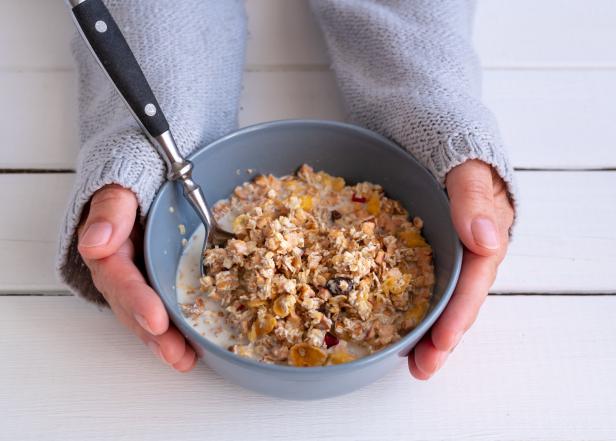 Zwei Hände, die eine Schüssel Müsli halten.