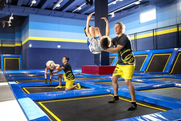 Zwei Trainer helfen Kindern beim Trampolinspringen in einer Trampolinhalle.