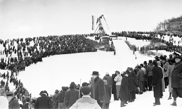 Eine große Menschenmenge versammelt sich an einem verschneiten Hang für ein Skispringen.