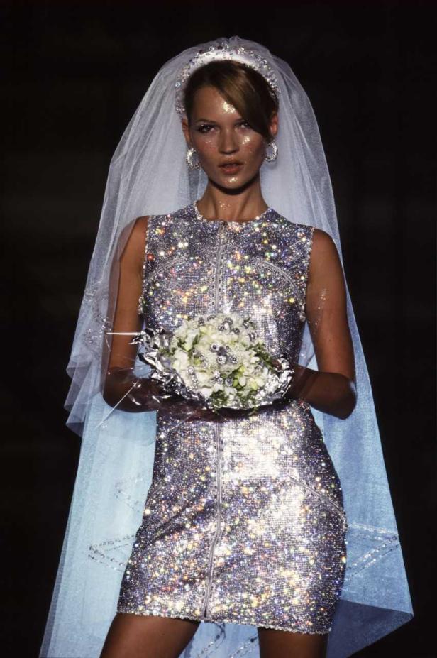 Kate Moss in einem glitzernden Minikleid und Schleier mit einem Blumenstrauß.