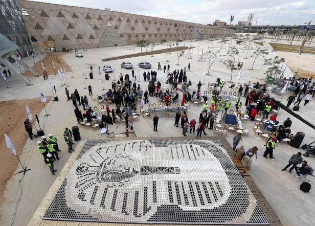 Eine große Menschenmenge versammelt sich vor dem Grand Egyptian Museum, vor einem Mosaik aus Tutanchamuns Maske.