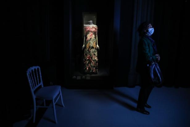 Eine Frau mit Maske betrachtet ein ausgestelltes, buntes Abendkleid in einem Museum.