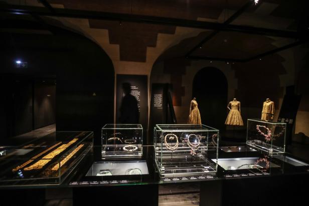 In einem Museum sind Schmuckstücke in Vitrinen und Kleider auf Schaufensterpuppen ausgestellt.