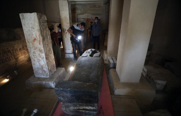 Besucher betrachten einen Sarkophag in einem ägyptischen Grab mit Hieroglyphen an den Wänden.