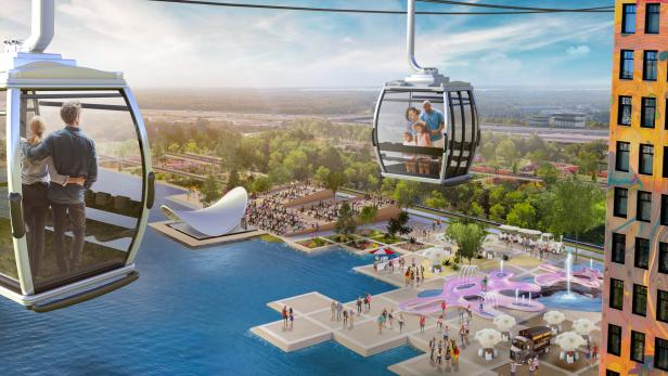 Eine Gondelbahn schwebt über einen Park mit Menschen, Wasserflächen und einem Gebäude.