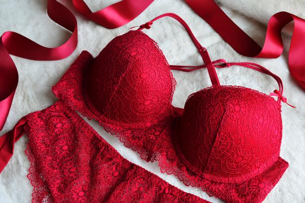 Ein rotes Spitzen-Dessous-Set liegt auf einem weißen, flauschigen Untergrund, dekoriert mit einer roten Schleife.