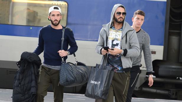 Drei Männer mit Taschen stehen vor einem Zug.