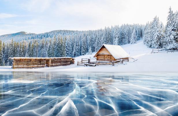 Eine verschneite Landschaft mit einer Holzhütte und einem Eissee im Vordergrund.