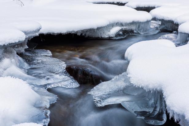 Ein Bach fließt durch eine verschneite und vereiste Winterlandschaft.