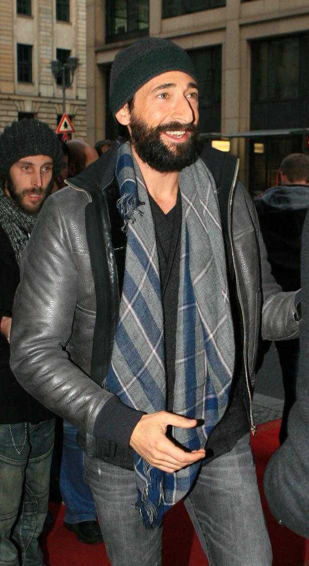 Adrien Brody mit Bart, Mütze und Schal auf dem roten Teppich.