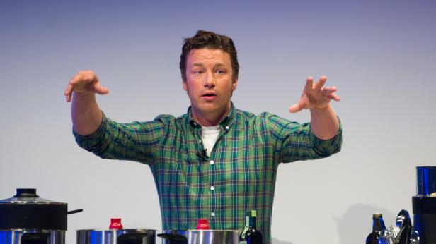 Jamie Oliver gestikuliert während einer Kochvorführung vor Töpfen.
