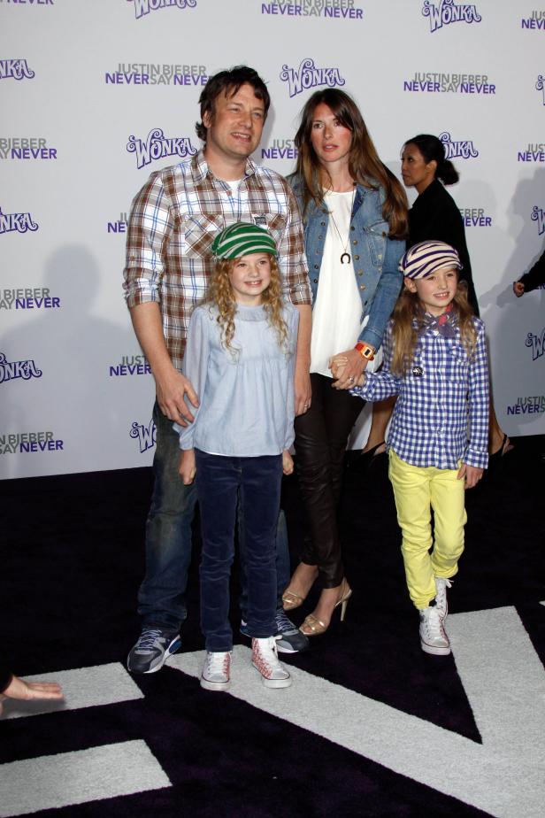 Jamie Oliver mit seiner Frau und seinen zwei Töchtern auf einem Event mit „Wonka“- und Justin Bieber-Hintergrund.