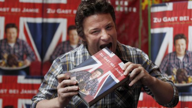 Jamie Oliver posiert mit seinem Buch „Zu Gast bei Jamie“.