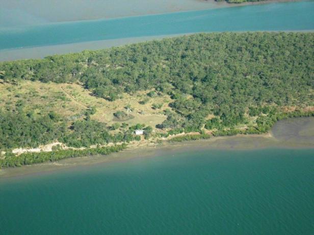 Luftaufnahme einer bewaldeten Insel, umgeben von türkisfarbenem Wasser.