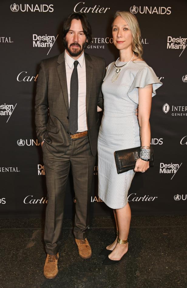 Keanu Reeves mit einer Frau auf einer Veranstaltung mit Sponsorenlogos im Hintergrund.