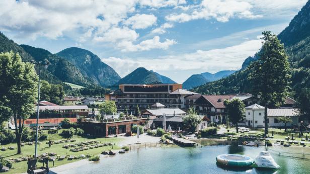 Ein Hotelresort liegt an einem See vor einer Bergkulisse.