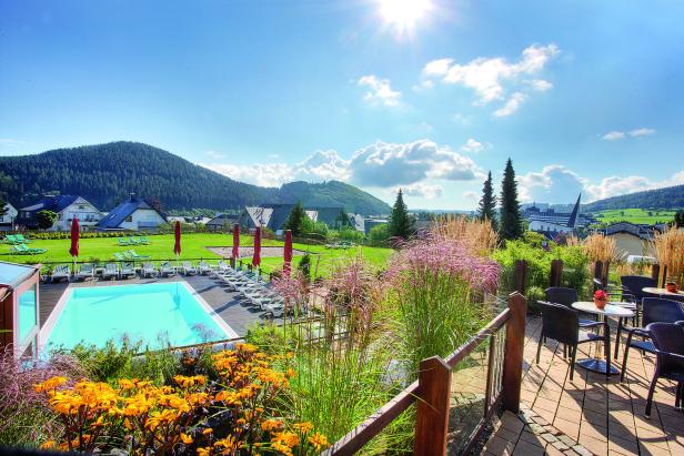 Ein Schwimmbad mit Liegestühlen und Sonnenschirmen vor einer grünen Hügellandschaft.