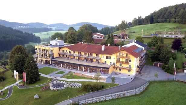 Ein gelbes Hotel mit roten Dächern liegt in einer grünen Hügellandschaft.