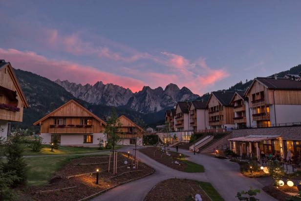 Häuser im alpenländischen Stil vor einer Bergkulisse bei Sonnenuntergang.