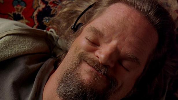 Jeff Bridges als „The Dude“ schläft mit Kopfhörern auf einem Teppich.
