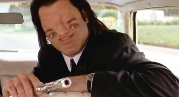 Ein Mann mit verzerrtem Gesicht hält eine Waffe in einem Auto.