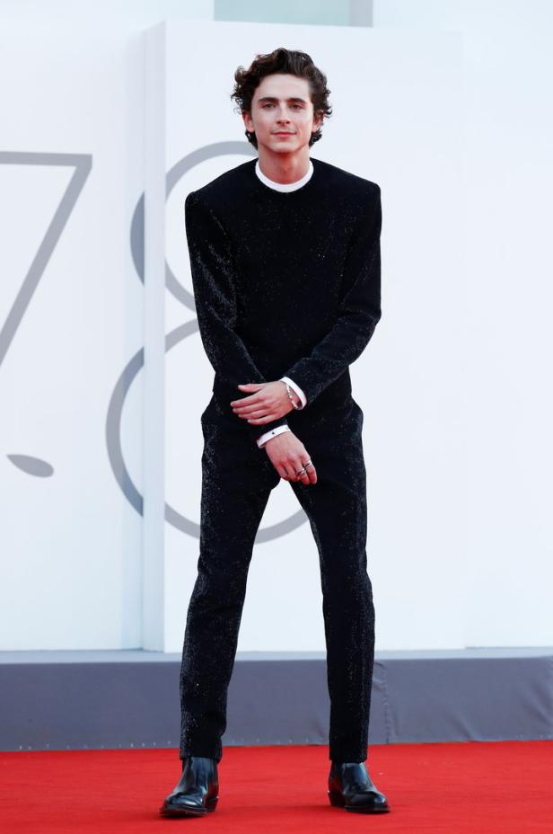 Timothée Chalamet posiert auf dem roten Teppich in einem glitzernden schwarzen Anzug.