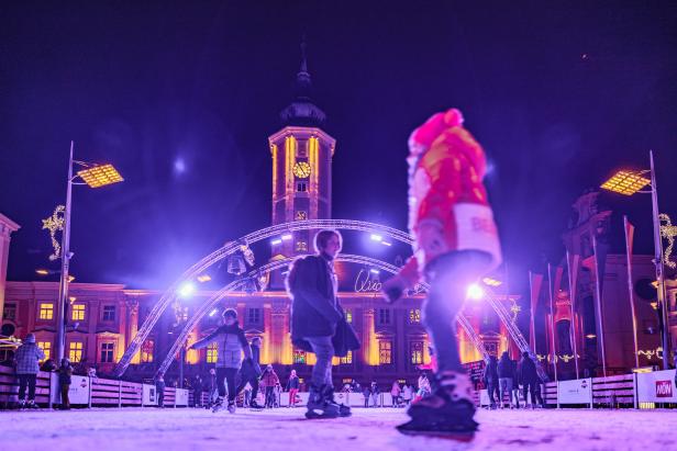 Menschen laufen auf einer Eisbahn vor dem Rathaus in Wiener Neustadt.